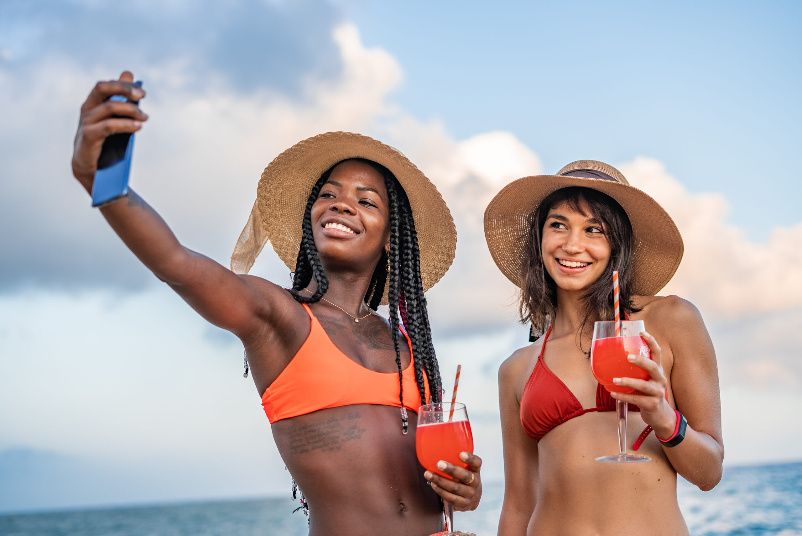 Diverse millennial girlfriends taking selfie during summer vacation, enjoying drinks.