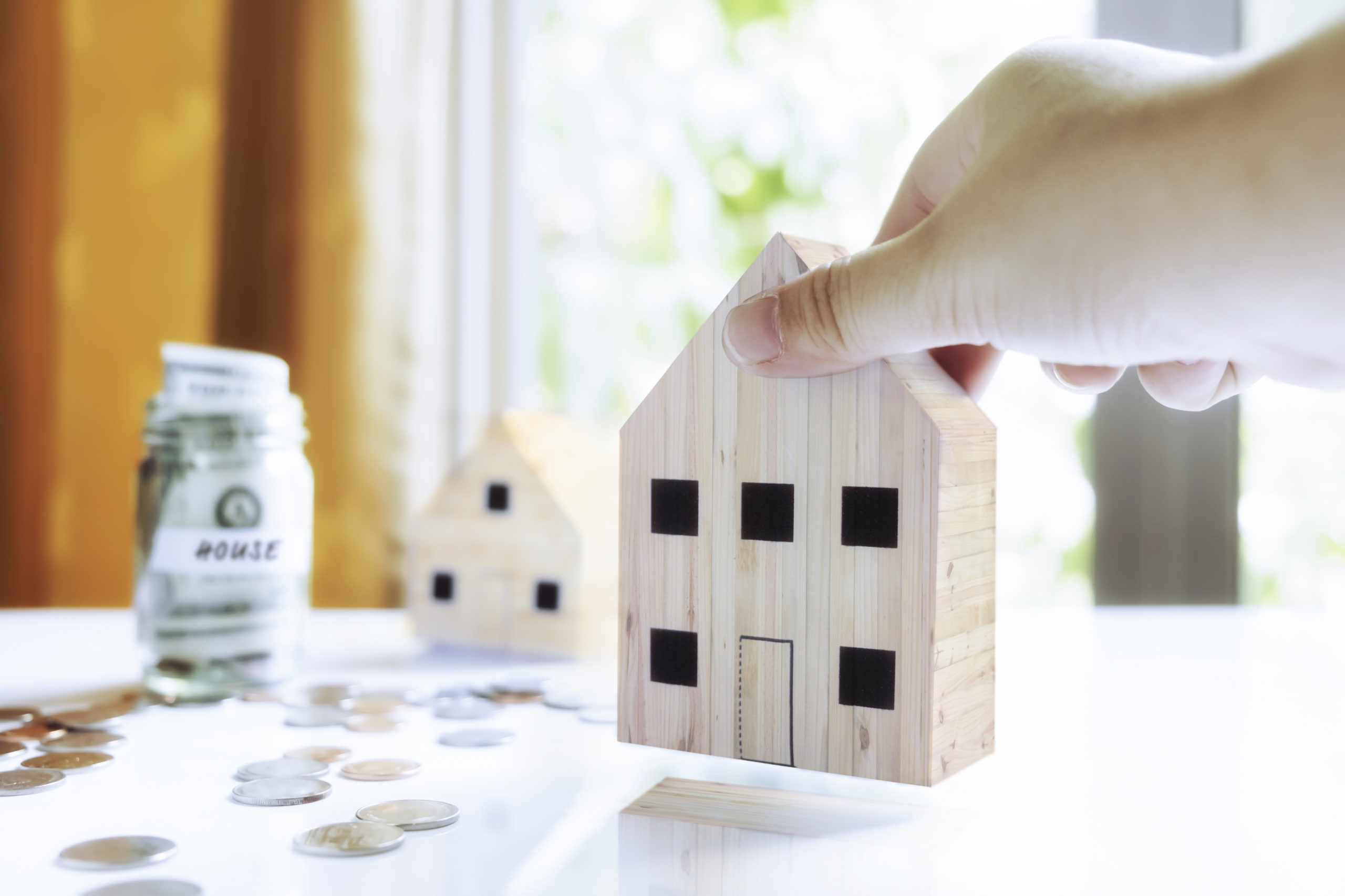 Hand holding miniature house model and coins representing home loans and mortgages